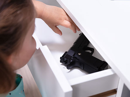 young girl reaching for a handgun in a drawer at home