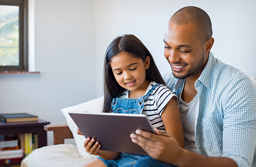 Father holding daughter on his lap to watch a video on a laptop computer